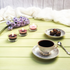 Cup of black coffee, candles and flowers on a wooden background.