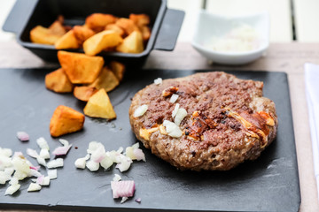 Grilled minced steak of beef with onions and fried potatoes on a