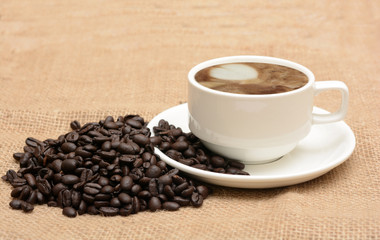 Coffee in cup with roasted beans on jute fabric background