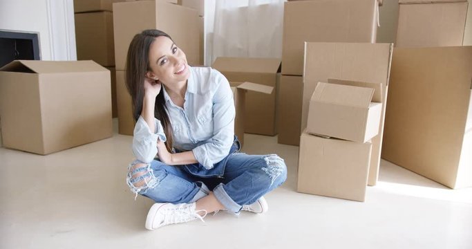 Happy young woman chatting on her mobile as she relaxes on the floor of the living room surrounded by boxes while moving home