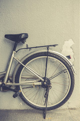 A bicycle parking in front of a peeling wall. Detail of a part of a bicycle leaning against a peeling wall. Vintage effect.