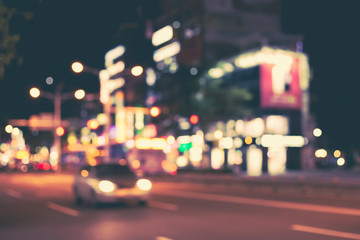 Blurred image of night city. Vehicles and motorcycles on the road. Shop signs with red, yellow, blue, brown colors. Retro effect.