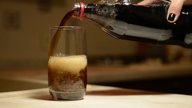 Close up shot of a highball glass in which a cola soda pop drink is poured.