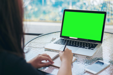 Mockup image of a woman writing and using laptop with blank green screen by swimming pool