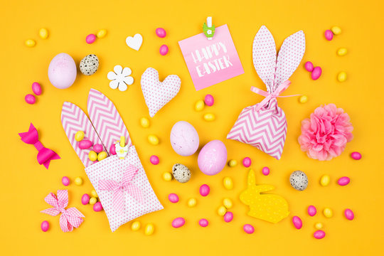 Easter holiday concept with pink and yellow Easter eggs, fabric bunny gift bags with candies and decoration