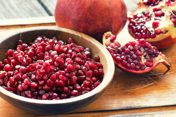peeled pomegranate and whole with garnet grains in a bowl on wooden background