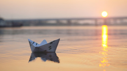 Man's hand putting paper boat on the water and pushing it away during beautiful sunset with reflection sun in the sea