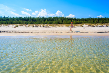 Young woman in swimsuit standing on Bialogora beach with crystal clear water, Baltic Sea, Poland
