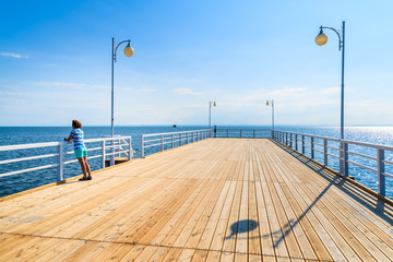 Wooden pier and young woman standing against railing in distance in Jurata town on coast of Baltic...