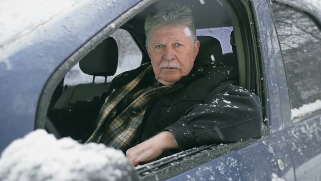 old man sitting in car, snow falls, slow motion