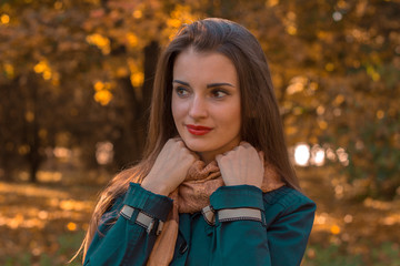 young girl stands in the park looks away and keeps hands for scarf