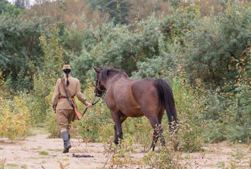 A woman in a uniform walking with a horse in the woods.
