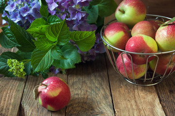 Apples in an iron vase and on a wooden surface.