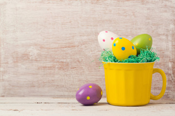 Easter holiday concept with egg decoration in yellow cup over rustic background