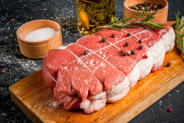 Fresh uncooked roastbeef on a cutting board with salt, pepper and rosemary for cooking. Close view
