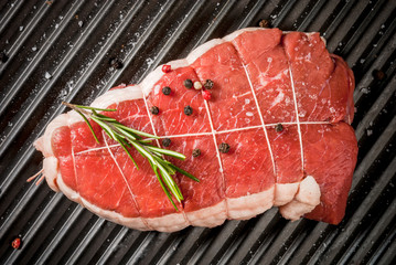 Fresh uncooked roast beef on on grill pan with salt, pepper and rosemary for cooking. Top view