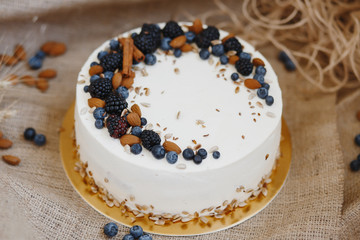 Delicate cake decorated with cinnamon sticks, nuts, blueberries and blackberries on a background of kraft paper and burlap.