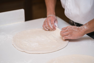 A pair of female hands are kneading bread dough into a pizza form.
