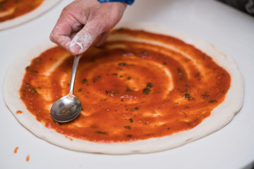 Pizza making in a restaurant, putting tomato sauce
