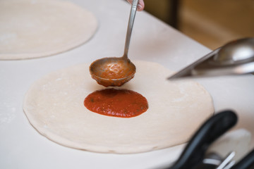 Pizza making in a restaurant, putting tomato sauce
