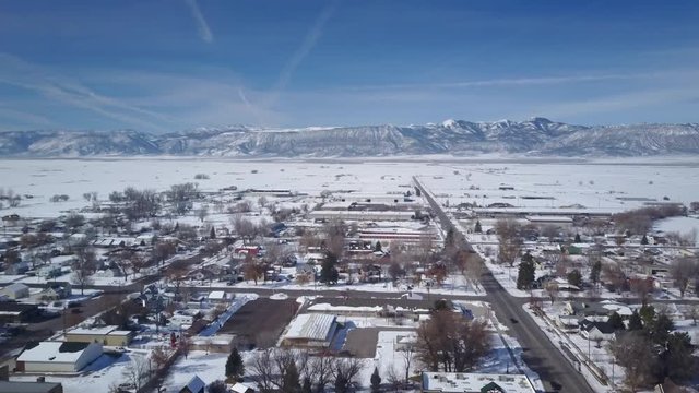 Aerial Ephraim Utah rural city climb over town. Winter storm blizzard snow. Rural farm community. Homes, barns and building. Hard seasonal weather. Hazard to driving. Surveillance spy. Drone flight.