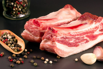 piece of pork on a dark background with peppercorn and garlic