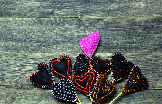 Handmade felt hearts on dark old wooden background. One heart different colors. Love card for Valentine's day. Concept with big copyspase for hand crafts or DIY illustration.