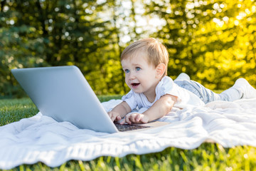 Cute baby boy playing with laptop and toys outdoors on green gra