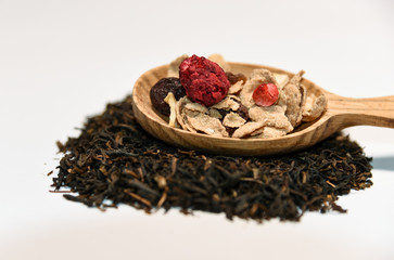 close up of oat cereals with dried red fruit and raisins served on a wooden spoon on loose black tea on white background