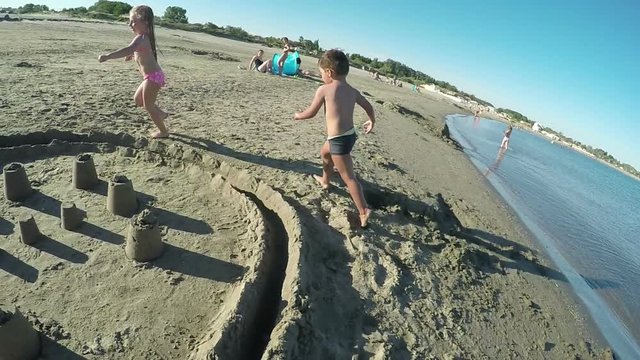 Little beautiful girl and boy running around on the sand sand castle