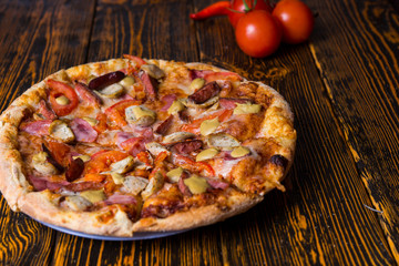 Close up of pizza with ham, tomatoes, sausages and sauce, near a