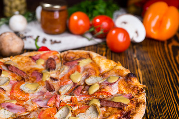 Close up of pizza on wooden table, tomatoes and other vegetables