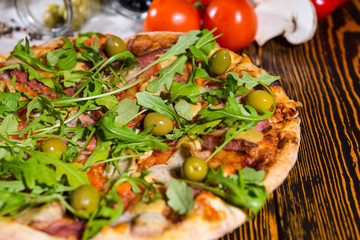 Close up of pizza with arugula and olives on wooden table