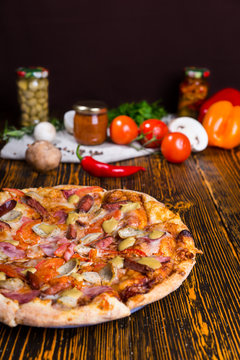 Pizza on wooden table, tomatoes and other vegetables in the back