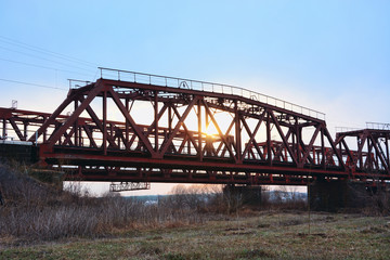 Old steel railway bridge on the river. Empty train-bridge in sunset 