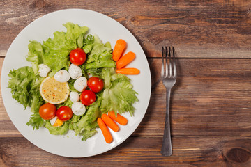 Tasty salad with cherry tomatoes, salad leaves, lemon, spices, carrot and quail eggs on wooden table with fork. Top view