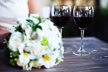 A bouquet of flowers and two glasses of wine on a wooden table.