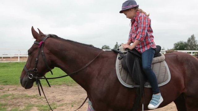 Little country girl trying to control the horse using a bridle while riding on horseback
