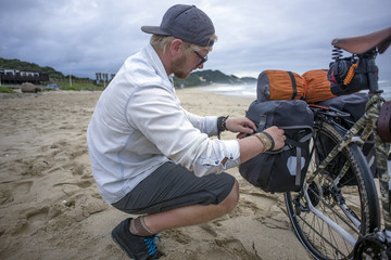 Long Distance Cyclist Prepares Panniers while on Beach