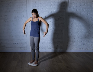 young fit and slim woman checking body weight on scale with big edgy shadow light sad and desperate