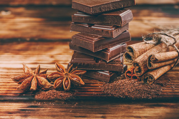 Broken chocolate bar and spices on wooden table. Selective focus