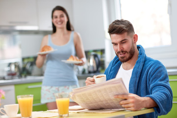 Man read newspaper and eat croissant in kitchen