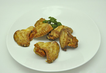 fried barbecue chicken wings with parsley on a white plate on a white background