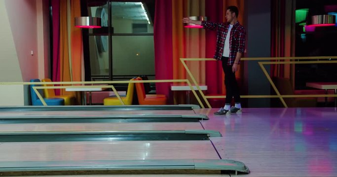 Young man playing bowling game and throwing ball to lane 4k leisure video. Guy rolling ball on alley. Hobby and competitions