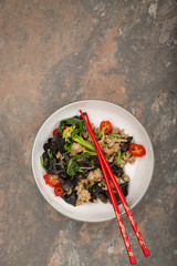 Wood ear mushroom stir-fry with ground meat and red peppers. Brown stone background. Red chopsticks placed in the bowl. 