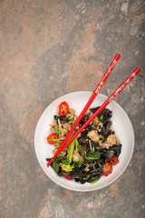 Wood ear mushroom stir-fry with ground meat and red peppers. Brown stone background. Red chopsticks on the top of the plate. 