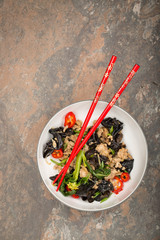 Wood ear mushroom stir-fry with ground meat and red peppers. Brown stone background. Red chopsticks on top of the plate