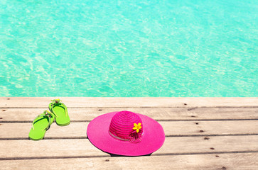 Fototapeta na wymiar Large pink sun hat and green flip plops on the deck by the sea