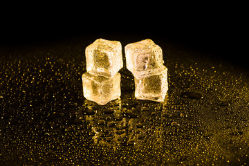 Ice cubes in yellow light on black wet table.