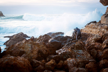 Brave photographer on the rocky beach with big splash